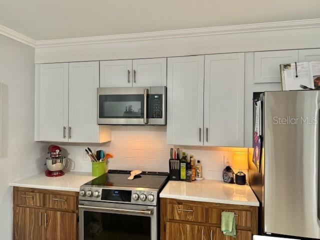 kitchen with backsplash, white cabinetry, ornamental molding, and appliances with stainless steel finishes