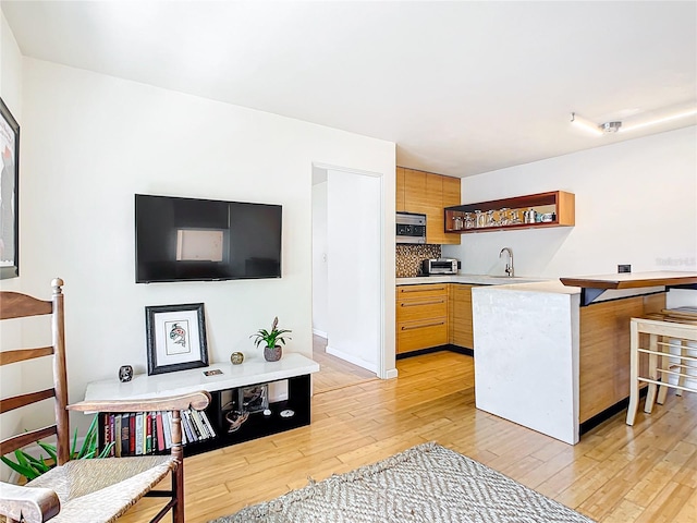 kitchen featuring kitchen peninsula, tasteful backsplash, light brown cabinetry, and light wood-type flooring