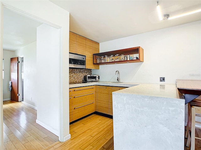 kitchen with kitchen peninsula, stainless steel microwave, backsplash, a breakfast bar area, and light hardwood / wood-style floors