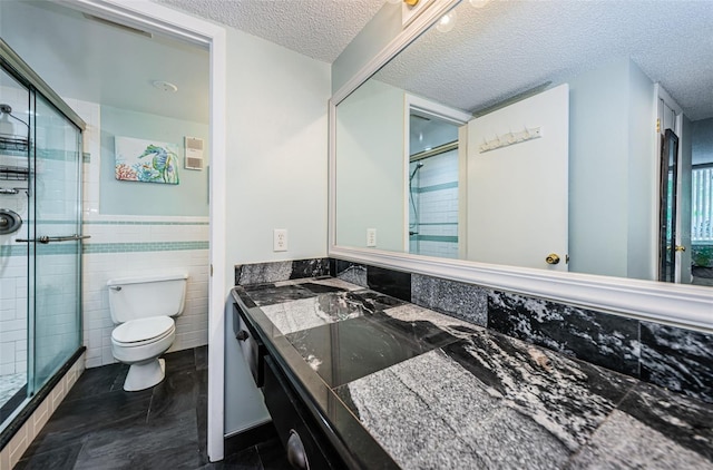 bathroom featuring an enclosed shower, vanity, a textured ceiling, tile walls, and toilet