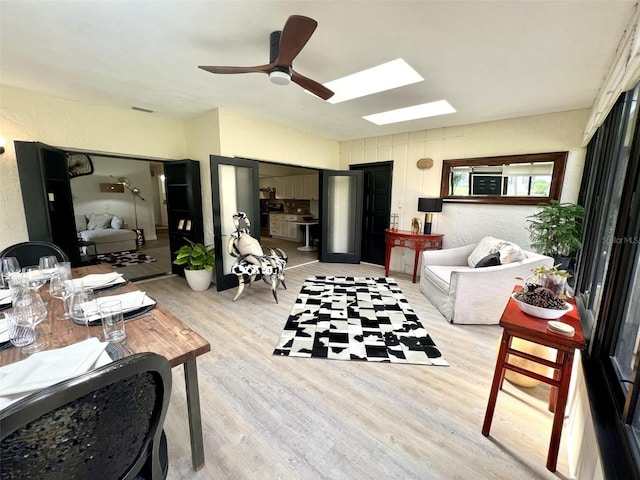 living room featuring ceiling fan, a skylight, and light wood-type flooring