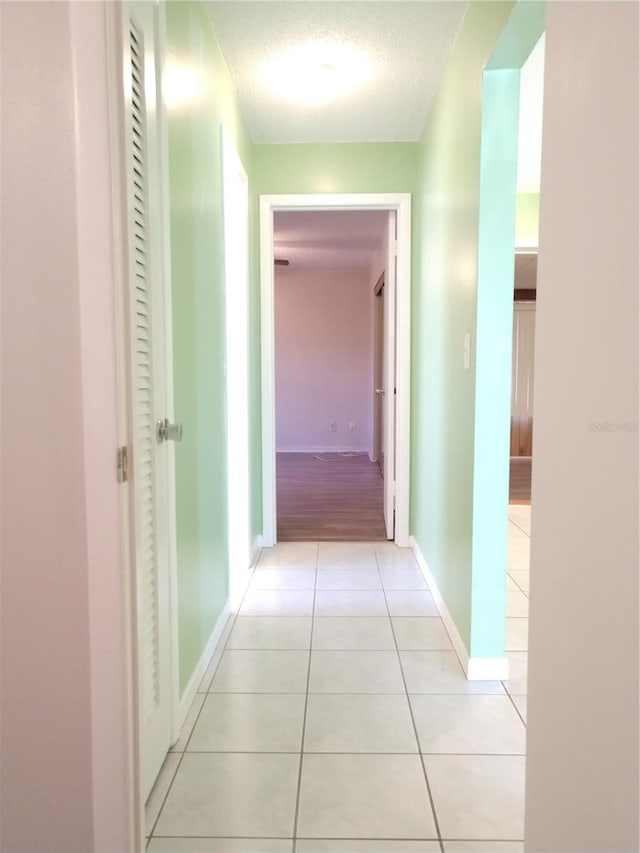 hall with a textured ceiling, baseboards, and light tile patterned floors