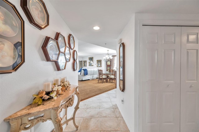 hall with light tile patterned floors, light colored carpet, baseboards, and an inviting chandelier