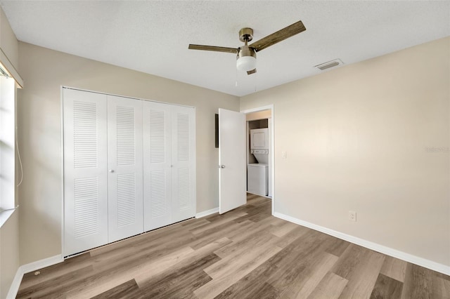 unfurnished bedroom featuring stacked washer / dryer, a closet, a textured ceiling, ceiling fan, and light hardwood / wood-style flooring