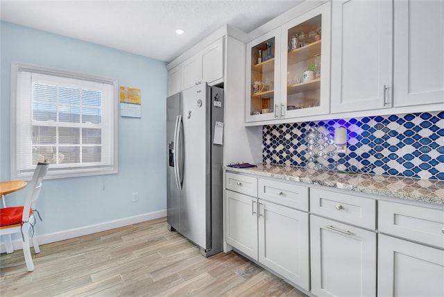 kitchen featuring white cabinets, stainless steel refrigerator with ice dispenser, decorative backsplash, and light stone countertops