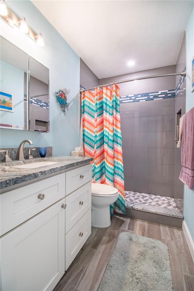 bathroom with a textured ceiling, vanity, hardwood / wood-style flooring, toilet, and curtained shower