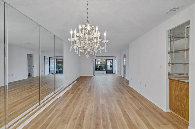 empty room with a textured ceiling, light wood-type flooring, and an inviting chandelier