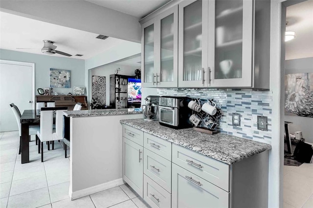 kitchen featuring gray cabinetry, ceiling fan, light tile flooring, light stone counters, and tasteful backsplash