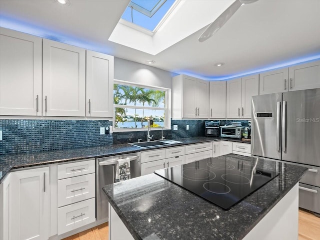 kitchen featuring dark stone countertops, a skylight, appliances with stainless steel finishes, and sink