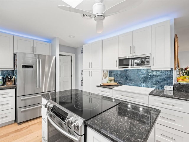 kitchen with dark stone countertops, white cabinetry, stainless steel appliances, ceiling fan, and light hardwood / wood-style flooring