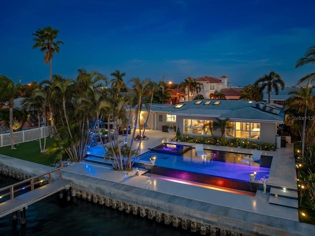 back house at night with a water view, a swimming pool with hot tub, and a patio area