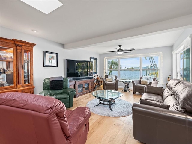 living room featuring a water view, beamed ceiling, ceiling fan, a skylight, and hardwood / wood-style flooring