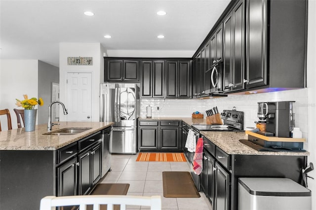 kitchen with light tile patterned floors, stainless steel appliances, tasteful backsplash, a sink, and dark cabinets