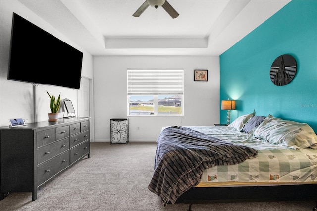 carpeted bedroom with a tray ceiling, ceiling fan, and baseboards