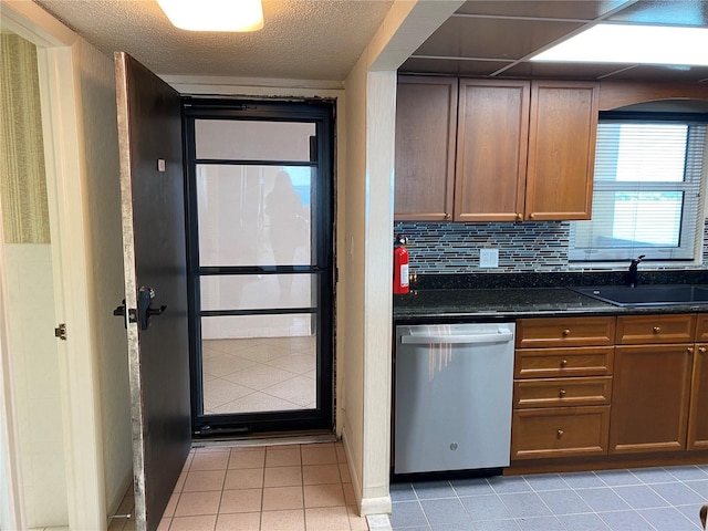 kitchen with dishwasher, sink, backsplash, dark stone counters, and light tile patterned flooring