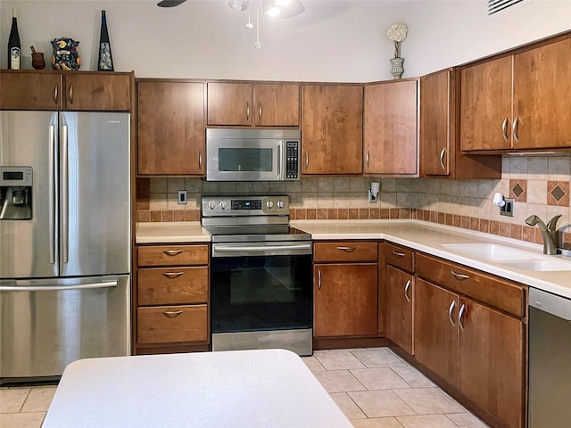 kitchen with ceiling fan, light tile flooring, sink, stainless steel appliances, and tasteful backsplash