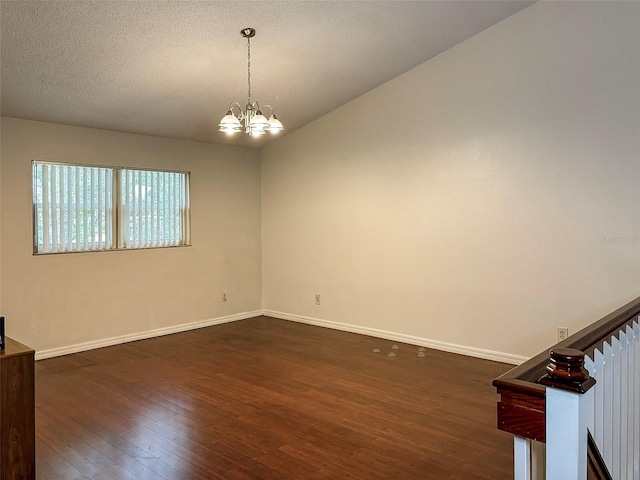 spare room with a textured ceiling, a notable chandelier, and dark hardwood / wood-style floors