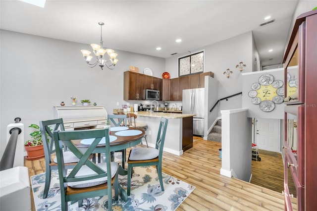 kitchen featuring light stone countertops, decorative light fixtures, stainless steel appliances, light hardwood / wood-style floors, and a notable chandelier