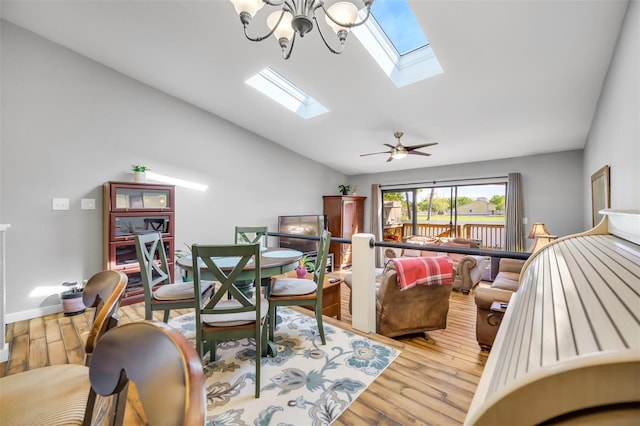 living room with ceiling fan with notable chandelier, light hardwood / wood-style floors, and vaulted ceiling with skylight