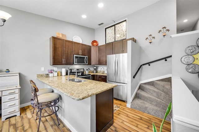 kitchen with sink, a breakfast bar area, stainless steel appliances, light hardwood / wood-style flooring, and kitchen peninsula