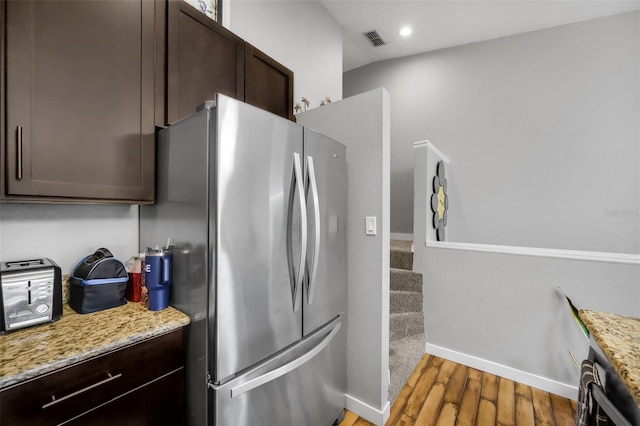 kitchen featuring dark hardwood / wood-style floors, dark brown cabinets, light stone countertops, and stainless steel fridge