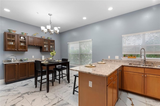 kitchen with light stone countertops, hanging light fixtures, a kitchen breakfast bar, sink, and light tile floors