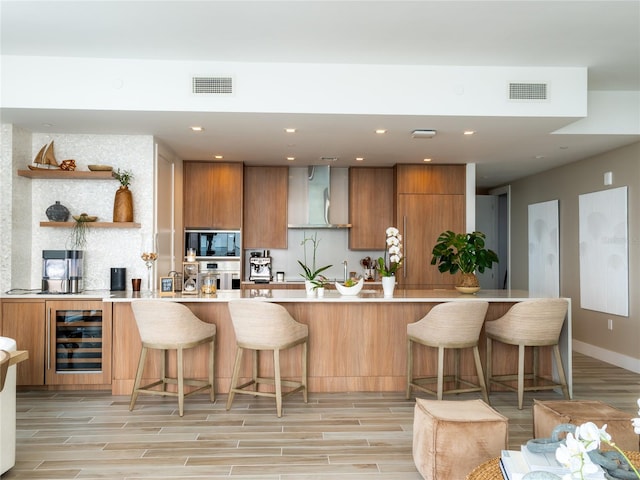 kitchen with oven, a kitchen breakfast bar, beverage cooler, wall chimney range hood, and black microwave