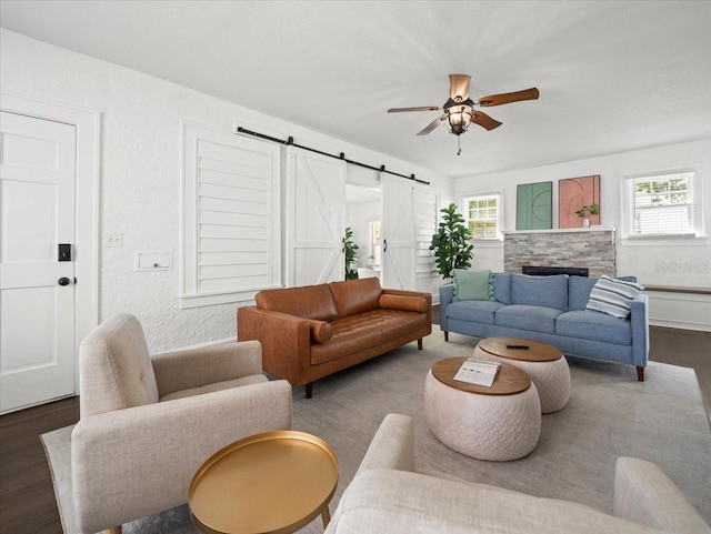 living room featuring a barn door, dark wood-type flooring, ceiling fan, and a wealth of natural light