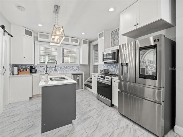 kitchen with a barn door, stainless steel appliances, white cabinetry, and sink