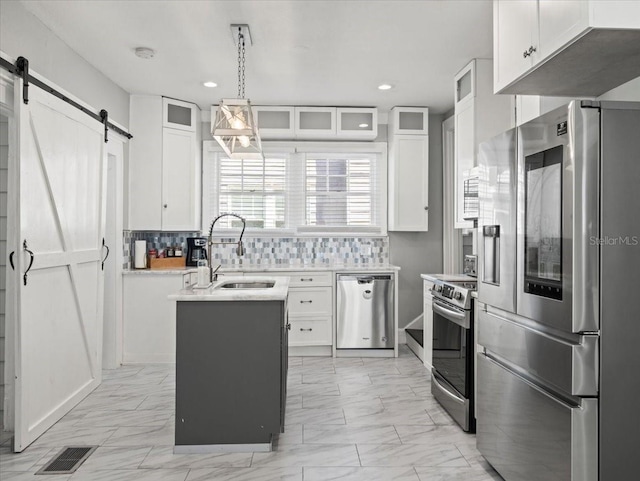 kitchen with pendant lighting, stainless steel appliances, a barn door, tasteful backsplash, and white cabinets