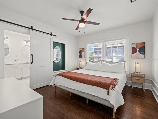 bedroom featuring a barn door, ensuite bathroom, dark hardwood / wood-style flooring, and ceiling fan