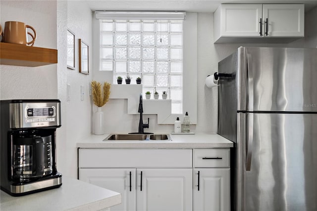 kitchen with stainless steel refrigerator, white cabinetry, and sink