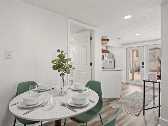 dining room with a textured ceiling, light hardwood / wood-style flooring, and french doors