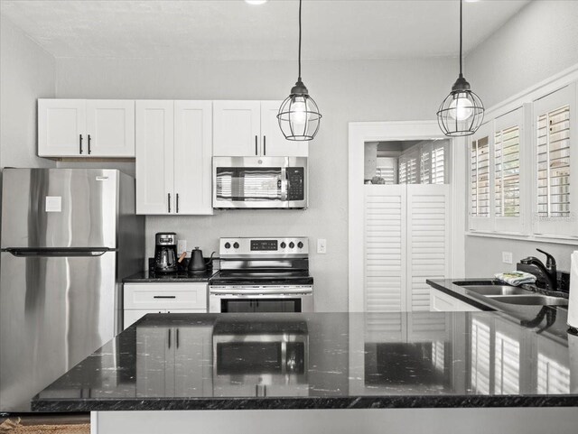 kitchen with stainless steel appliances, white cabinetry, and dark stone countertops