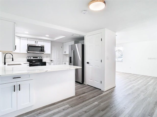 kitchen featuring appliances with stainless steel finishes, sink, kitchen peninsula, light wood-type flooring, and white cabinetry