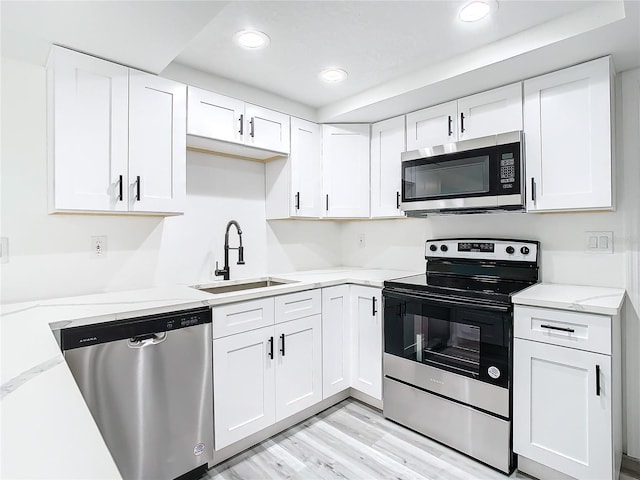 kitchen featuring white cabinetry, light wood-type flooring, light stone counters, stainless steel appliances, and sink