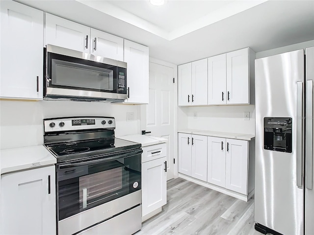 kitchen featuring white cabinets, light hardwood / wood-style flooring, appliances with stainless steel finishes, and a tray ceiling