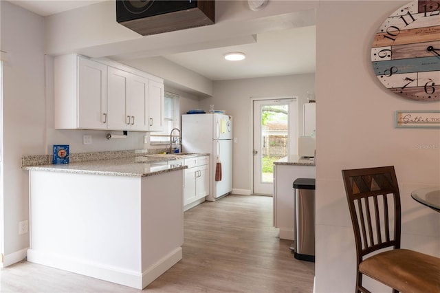 kitchen with white cabinets, white refrigerator, light stone counters, and light hardwood / wood-style flooring