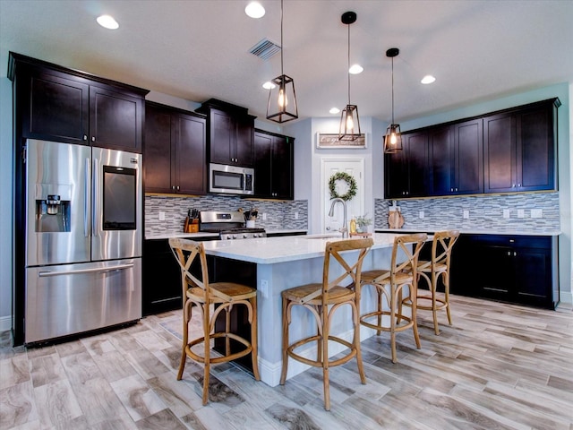 kitchen featuring an island with sink, pendant lighting, a kitchen bar, dark brown cabinets, and appliances with stainless steel finishes