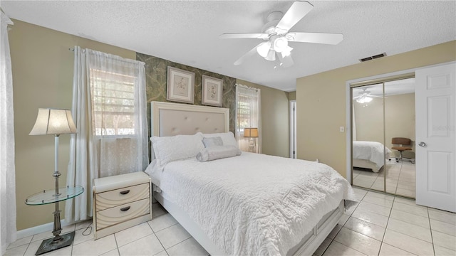 bedroom featuring ceiling fan, a closet, light tile floors, and a textured ceiling