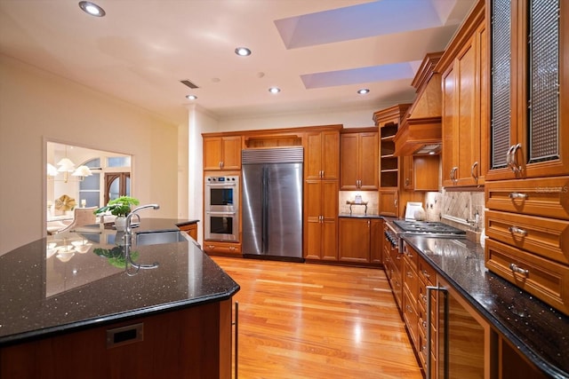 kitchen featuring stainless steel appliances, light wood-type flooring, tasteful backsplash, dark stone countertops, and sink