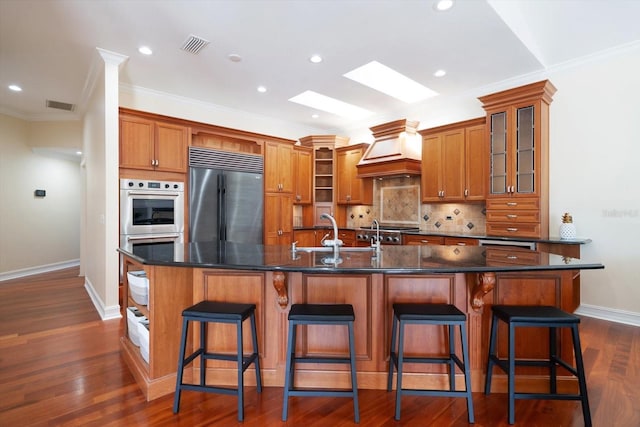 kitchen with appliances with stainless steel finishes, backsplash, dark wood-type flooring, custom exhaust hood, and a kitchen bar