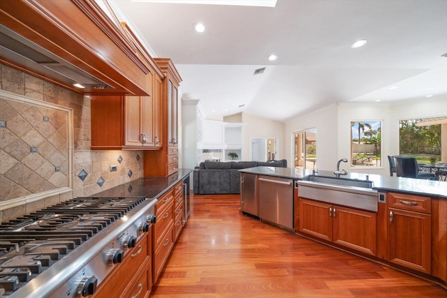 kitchen featuring sink, a healthy amount of sunlight, custom exhaust hood, tasteful backsplash, and light wood-type flooring