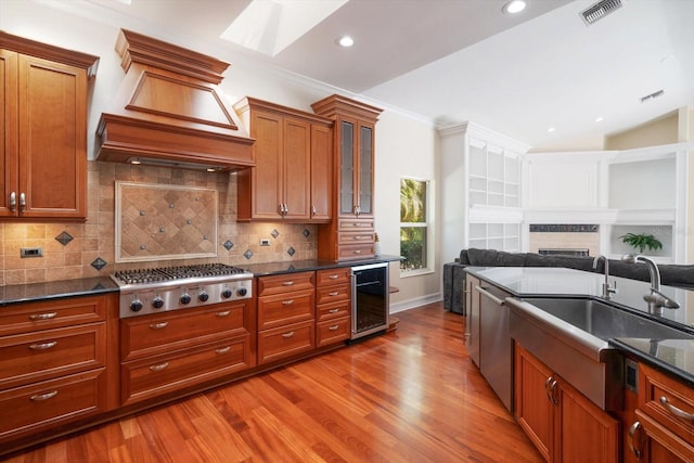 kitchen featuring dark stone counters, light hardwood / wood-style floors, custom exhaust hood, beverage cooler, and tasteful backsplash