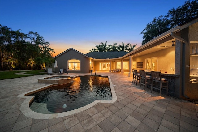 pool at dusk featuring an in ground hot tub and a patio area