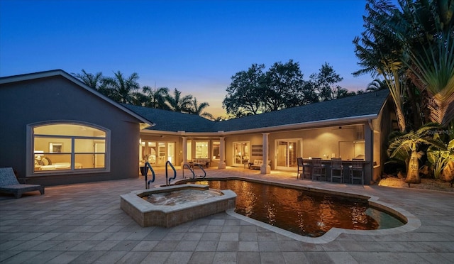 back house at dusk featuring a patio and a bar