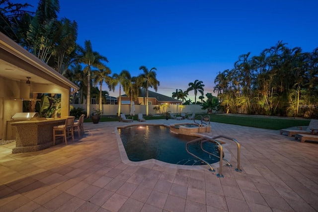 pool at dusk featuring a patio area and an in ground hot tub