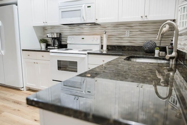 kitchen with light wood-type flooring, sink, white appliances, white cabinetry, and dark stone counters