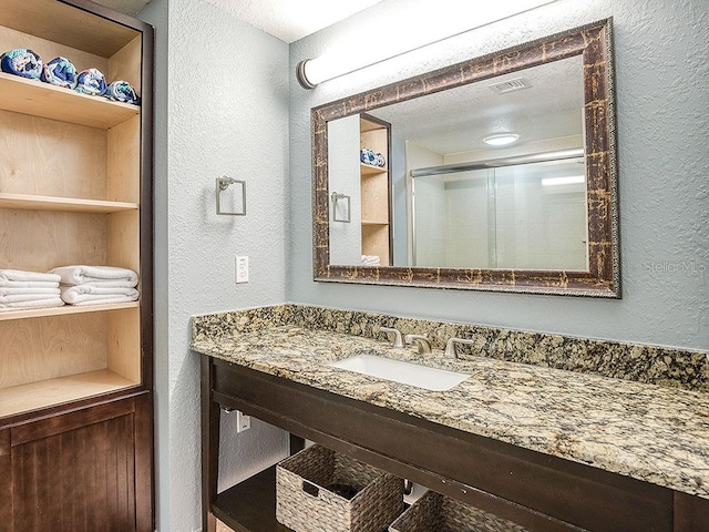 bathroom with a textured ceiling, vanity, and a shower with door