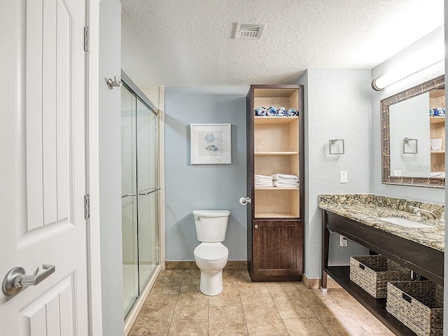 bathroom with vanity, toilet, a textured ceiling, walk in shower, and tile patterned flooring